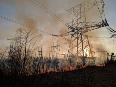 Burning electricity pylons at power plant at sunset. AEM wildfire risk management weather systems can help.
